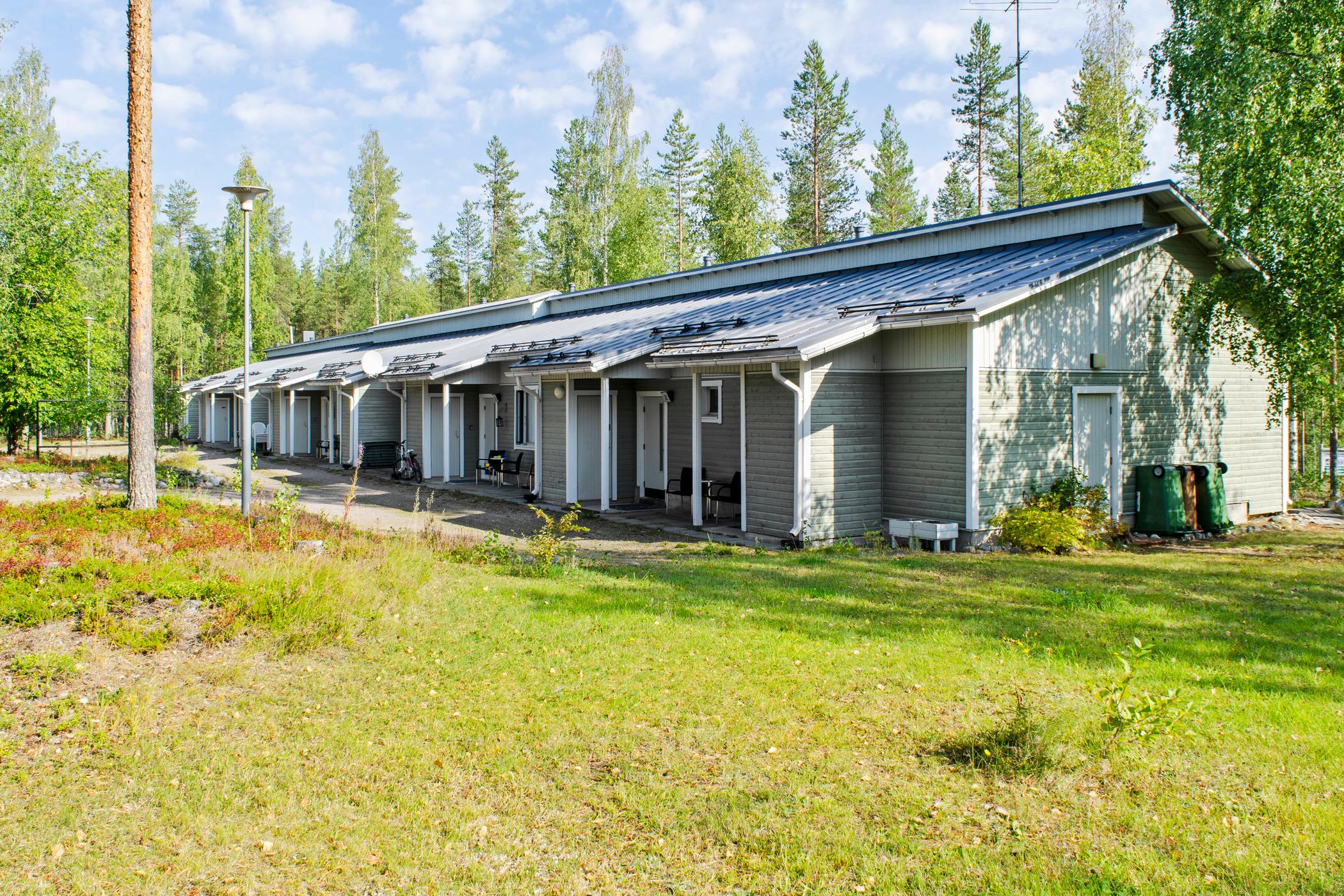 Light green/white terraced wooden house in summer light, with green grass in the foreground.